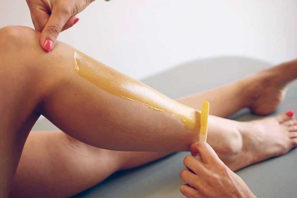 Applying wax to lower leg for hair removal with a wooden spatula.