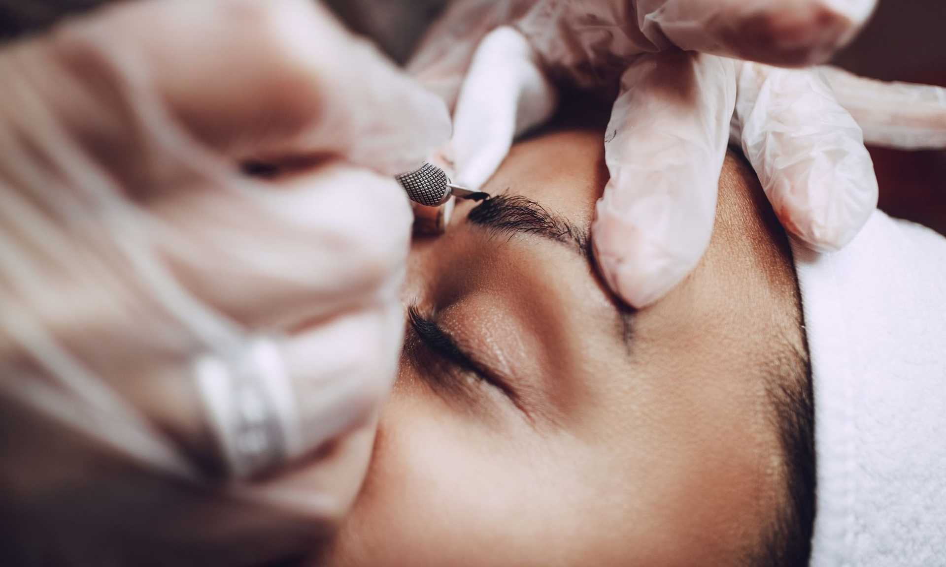Close-up of a person getting eyebrow microblading done by a professional with gloves.